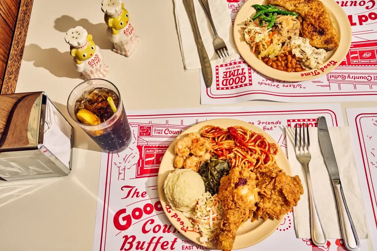 Plates of fried chicken, mac and cheese, collard greens, mashed potatoes and spaghetti on red and white Good Time Country Buffet placemats in the East Village
