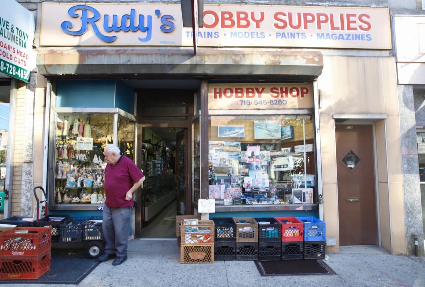 Rudy's Hobby & Art storefront on Astoria Blvd with the classic trains, models, paints, and magazines sign and crates of books out front