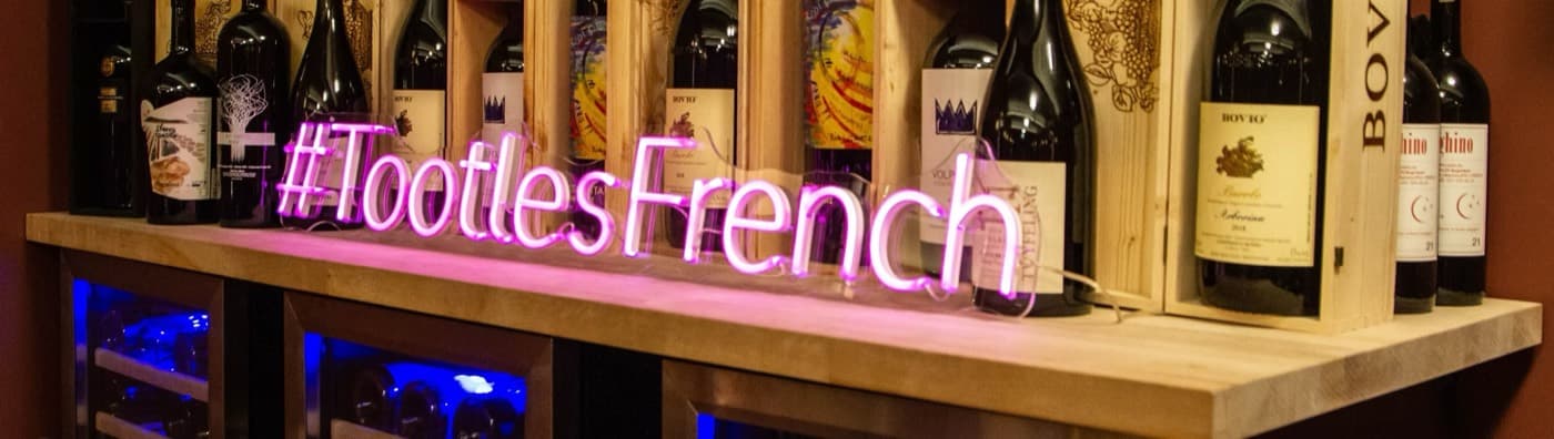 The neon #TootlesFrench sign glowing on the wine shelf at Tootles & French wine bar on Ditmars Blvd in Astoria