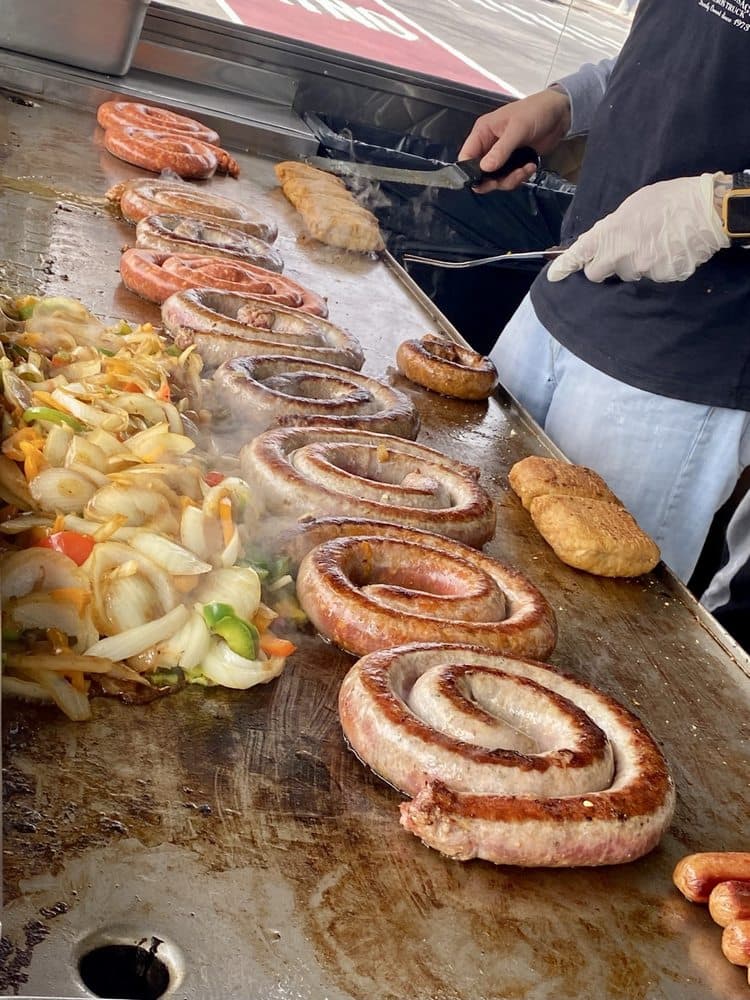 D'Angelo's Italian Sausage coiled fresh-link sausages searing on griddle with peppers and onions