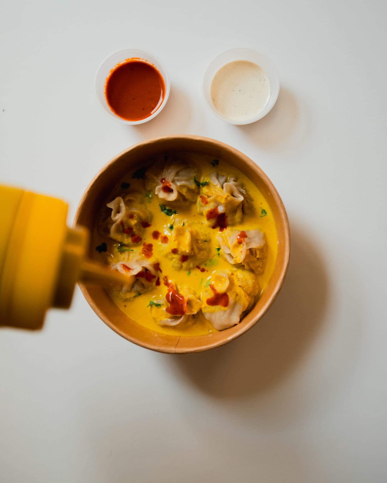 Dumpling Magic Tibetan momos in golden curry sauce with chili and white sauce sides