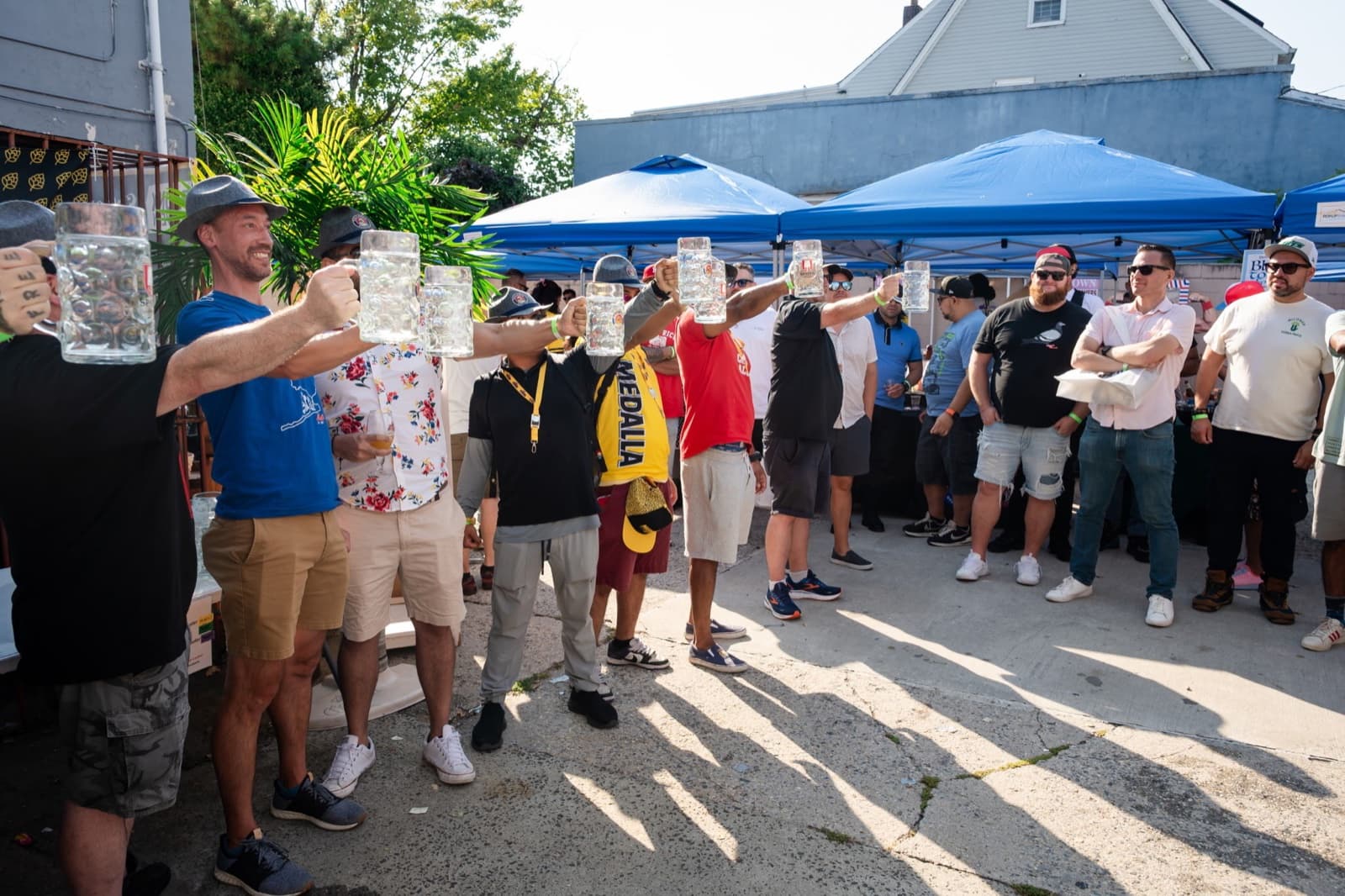 Crowd raising glass beer steins under tents at an outdoor beer festival