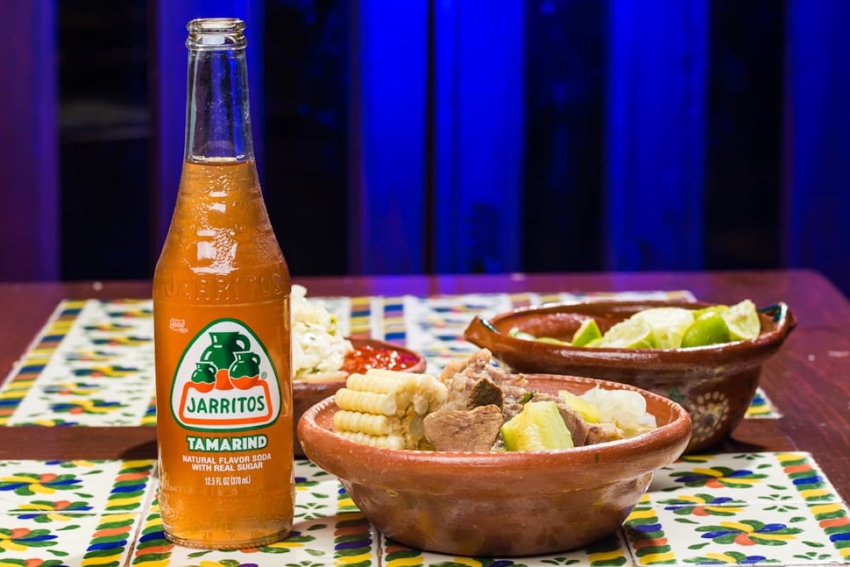 Birria with limes and a bottle of Jarritos tamarind soda on a festive tablecloth