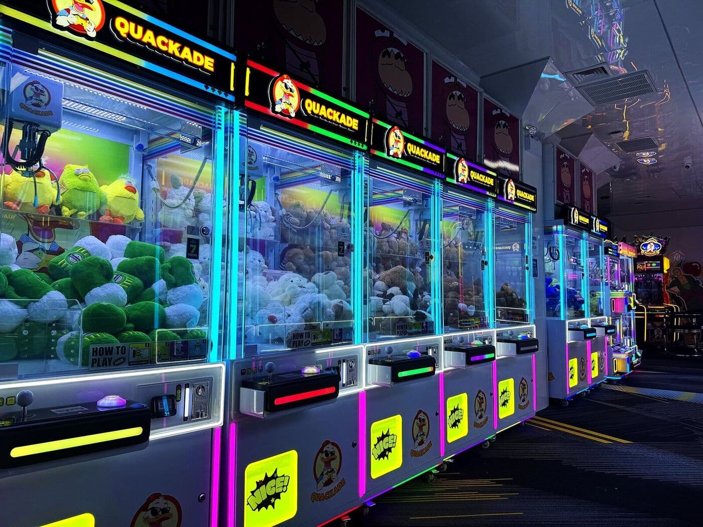 Neon lit row of Quackade claw machines packed with plush prizes at the duck themed arcade in Long Island City
