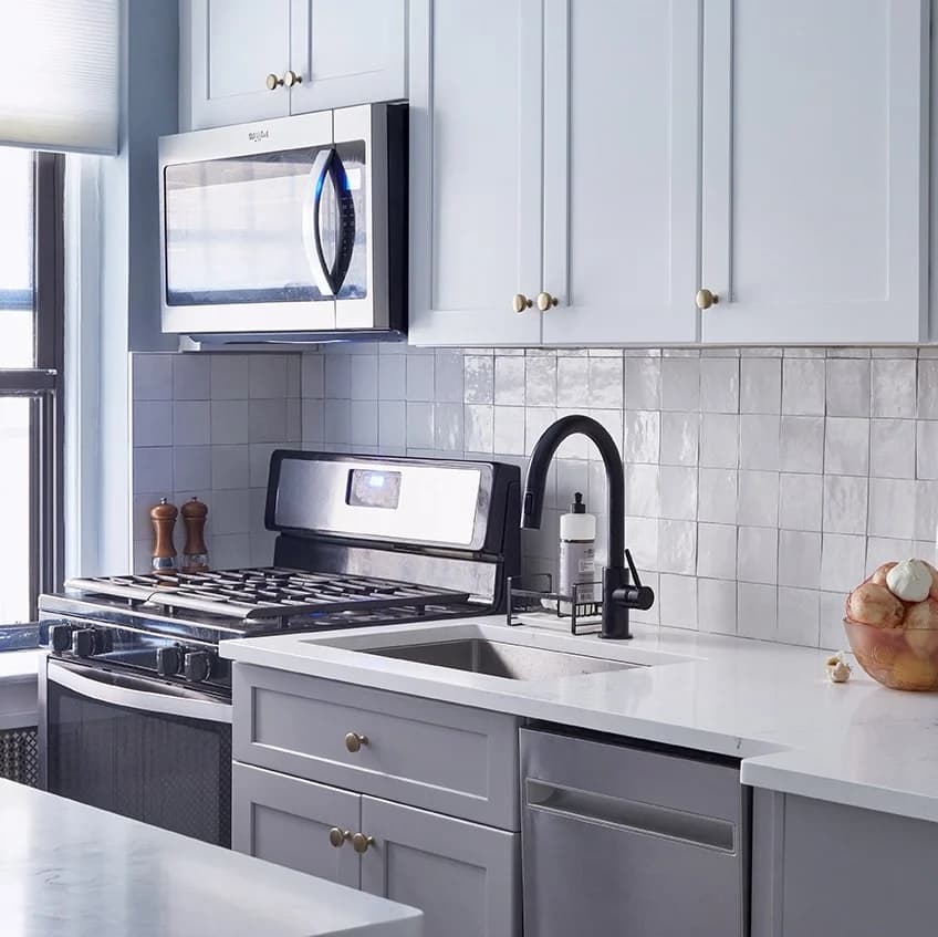 A bright home kitchen with white shaker cabinets, a glossy square tile backsplash, a gas range and a black faucet over the sink, the most exclusive restaurant in town