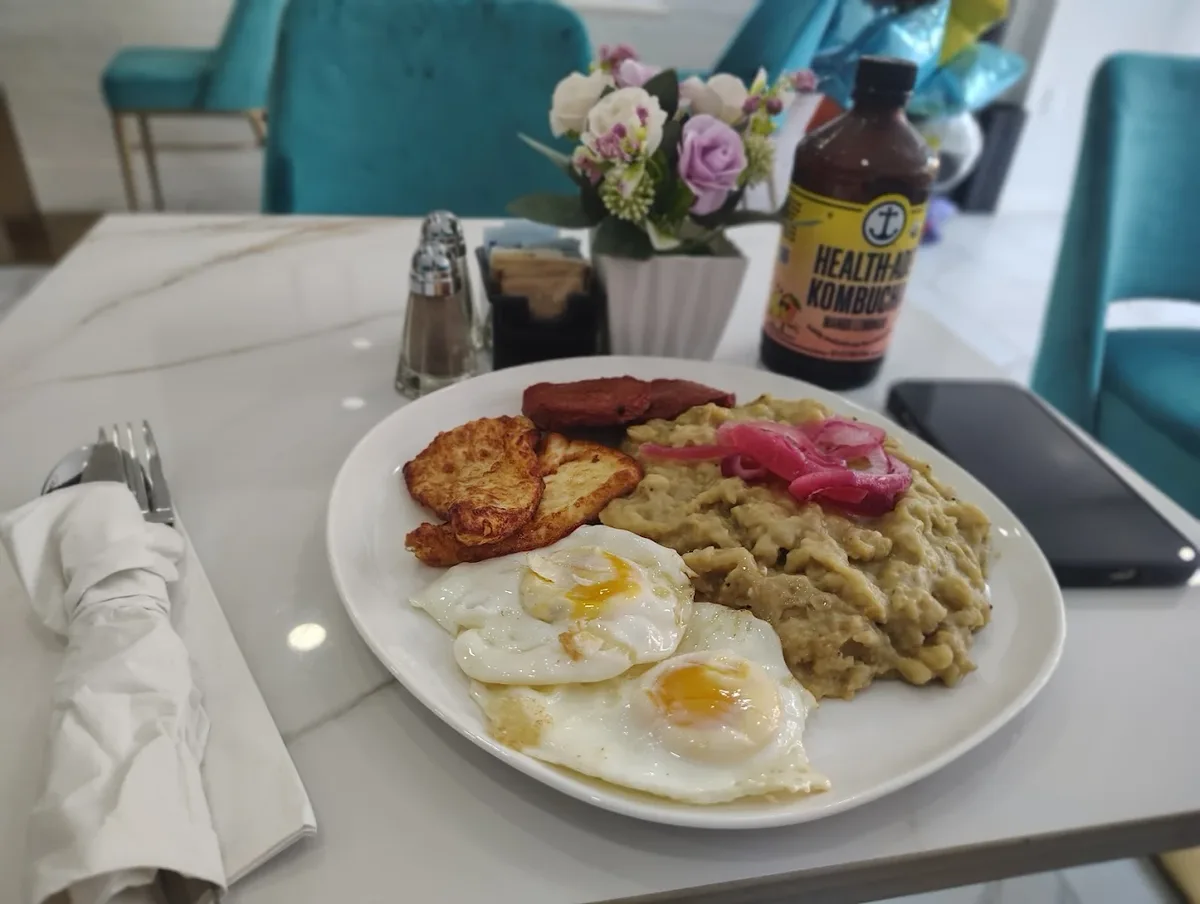 A Dominican breakfast plate of mangu topped with pickled red onion, two fried eggs, fried cheese and fried salami on a marble table