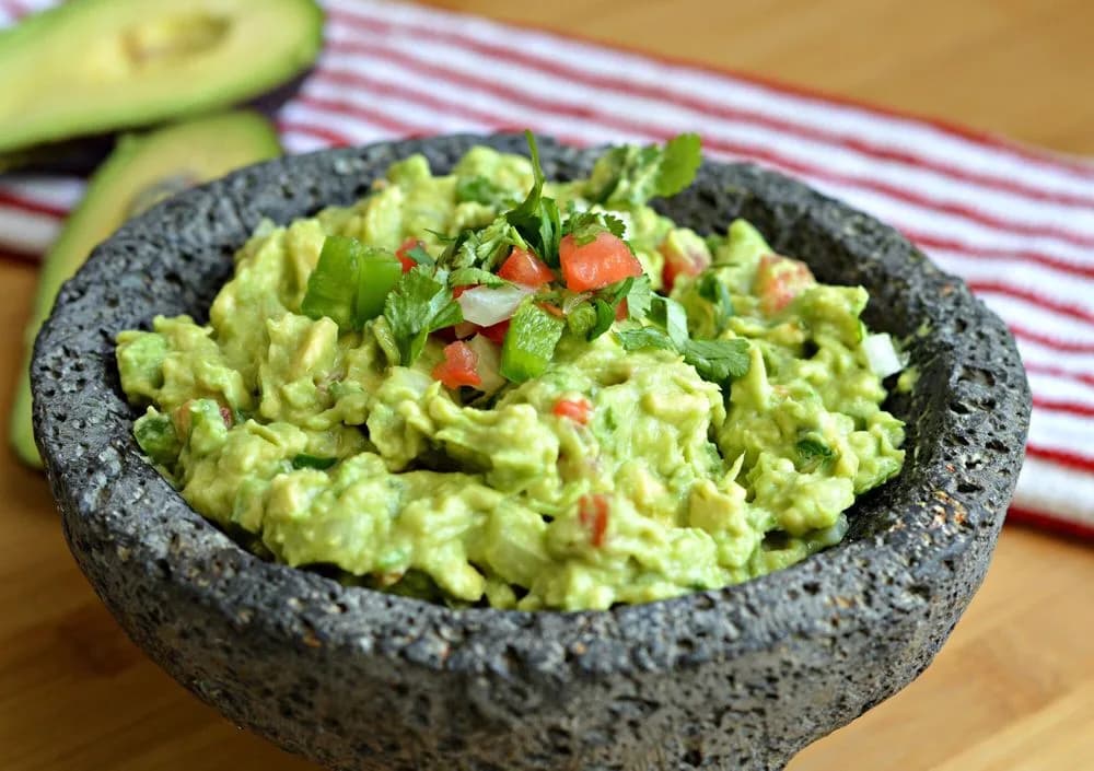 Fresh guacamole topped with diced tomato, onion, jalapeno and cilantro in a black lava stone molcajete