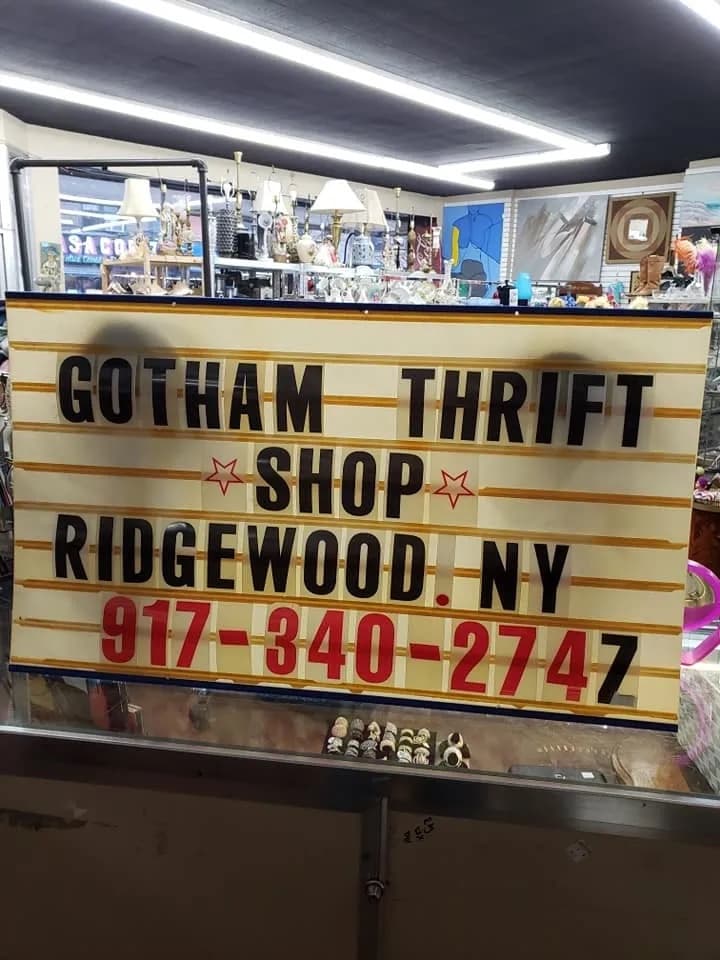 The Gotham Thrift Shop marquee sign in Ridgewood, NY, with lamps, art, and vintage finds filling the shelves behind it